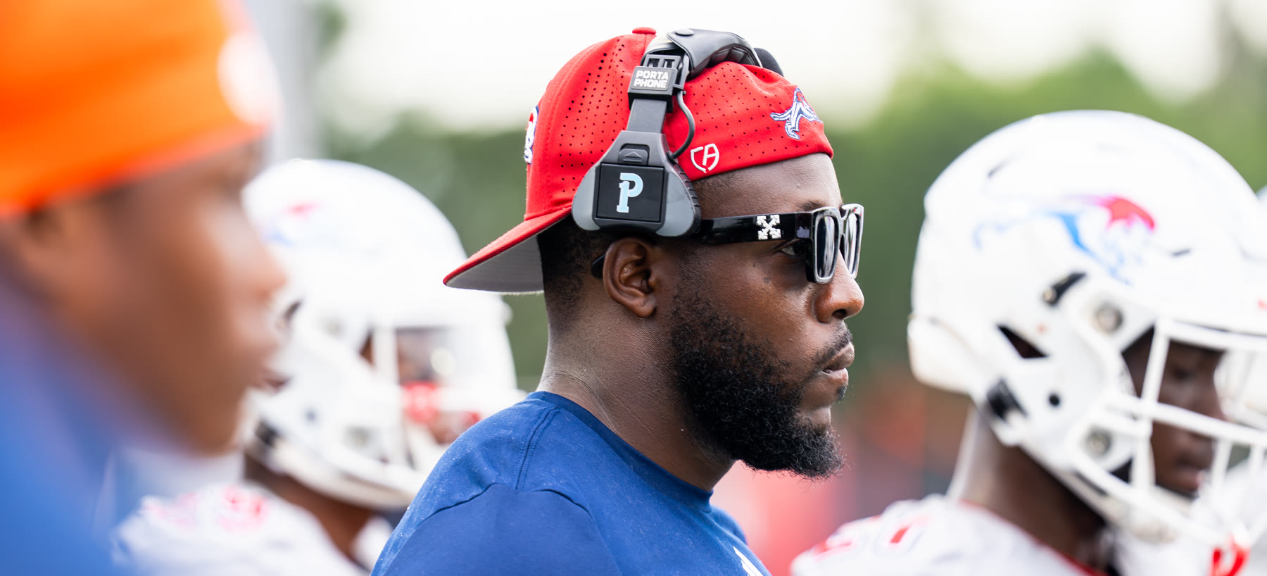 Coach Rick on the Chaminade-Madonna sideline during a game, players in helmets either side of him